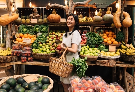 Side view of an Asian woman with a wicker shopping basket standing on a local outdoor market  Smiling female buying organic food
