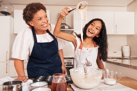 Grandmother and graddaughter having fun while preparing dough on kitchen  Happy girl with spoon