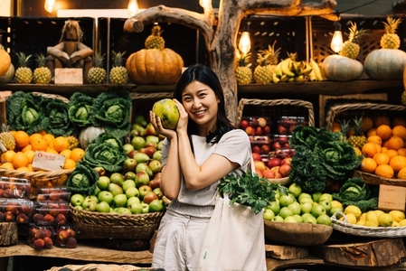 Cheerful woman holding fruit and looking at a camera while standing on a local outdoor market