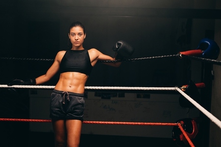 Sporty young woman standing against the ropes in a boxing ring