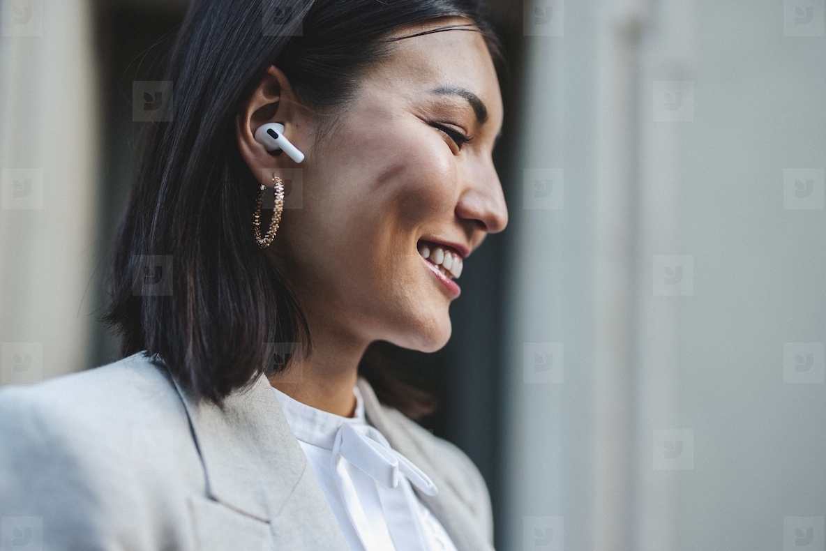 Business woman listening to music on wireless earphones in the street