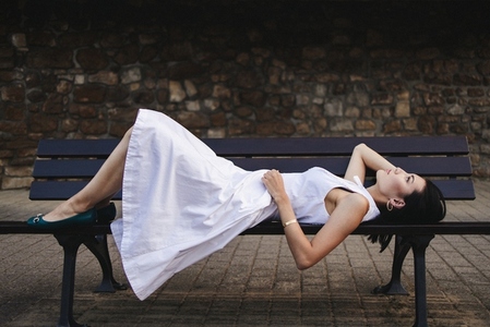 Woman lying on a bench in a dress outdoors