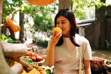 Asian woman with orange on an outdoor market  Young female smelling orange at market with organic food