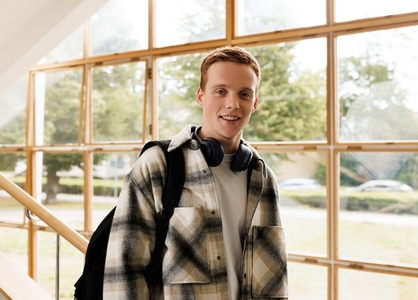 Portrait of a smiling male student standing against a window in college