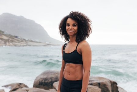 Portrait of a healthy woman with curly hair standing against the ocean after training