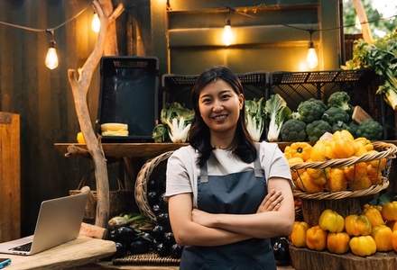 Portrait of an outdoor market owner  Asian woman with crossed arms wearing an apron standing against a stall