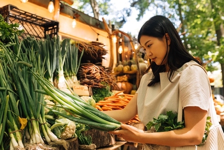 Asian woman holding a green onion  Female customer on an outdoor market