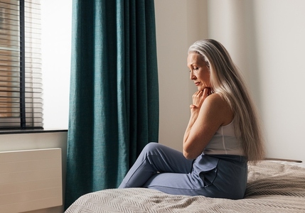 Sad senior woman sitting on a bed  Lonely depressed old female looking down in the bedroom