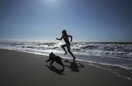 Girl and pet dog running on sunny ocean beach