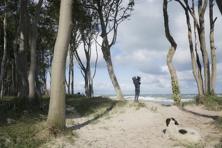 Girl holding pet dog on sunny ocean beach below trees