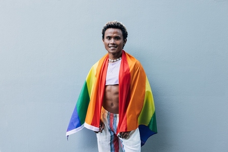 Young smiling male with LGBT flag at grey wall