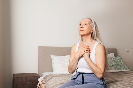 Worried senior woman sitting on a bed  Sad adult female with hands on chest