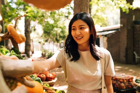 Young smiling woman in casuals buying fruits at a local market