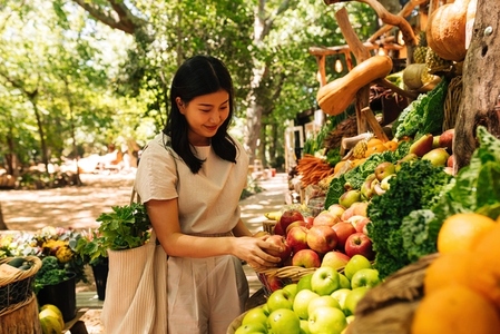 Smiling Asian woman choosing fruits  Female with a shopping bag at an outdoor market