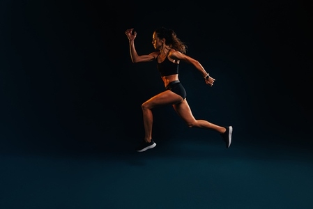 Sprinter against a black background  Muscular female running and jumping