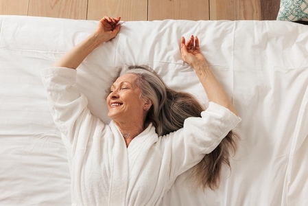 Smiling senior woman lying on bed with closed eyes enjoying morning