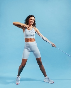Smiling woman exercising with elastic training band against a blue background