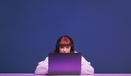 Woman with ginger hair looking at the camera while sitting behind her gaming laptop