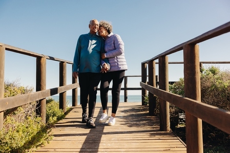 Senior couple walking along a wooden foot bridge at the beach