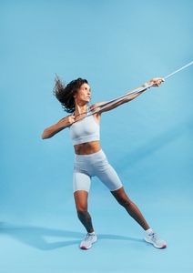 Full length of a slim woman in sportswear practicing on blue background with a resistance band