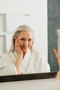 Aged woman in the bathroom looking at a mirror  Senior female in bathrobe doing morning routine