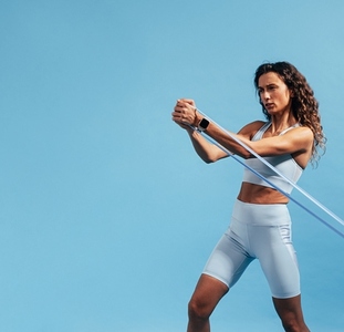 Slim woman in blue sportswear exercising with resistance band