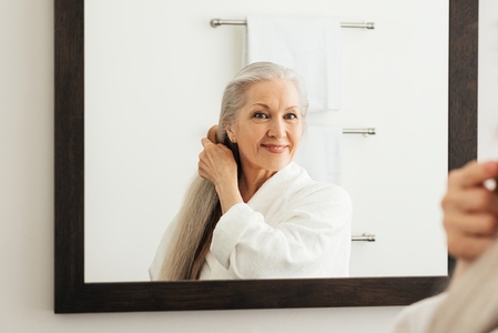 Portrait of a senior woman with a wood comb looking at a mirror  Aged female combing her beautiful long grey hair