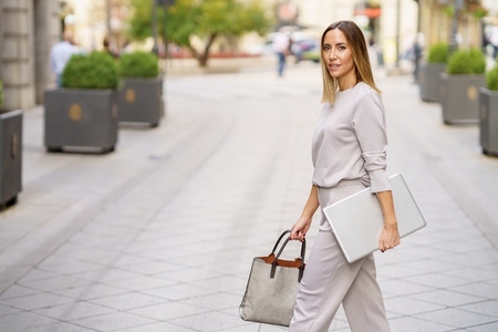 Stylish female entrepreneur with netbook strolling on city street