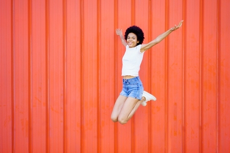 Carefree black woman jumping near wall