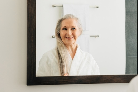 Smiling woman with long grey hair looking at a mirror in bathroom