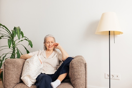 Aged smiling woman with grey hair relaxing in an armchair at home