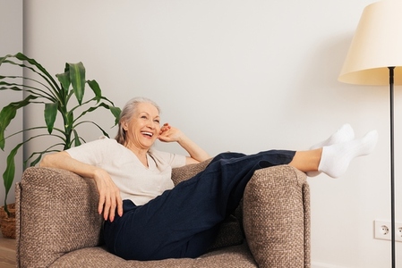 Laughing senior woman relaxing in an armchair at home  Aged female in casuals in living room
