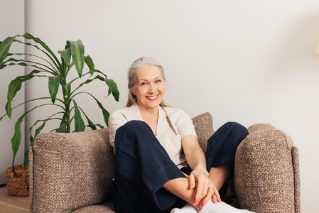 Portrait of a senior woman sitting on an armchair at home  Aged smiling female in casuals looking at camera in living room