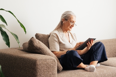 Aged female sitting on a couch using a digital tablet