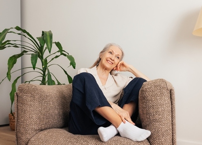 Cheerful senior woman relaxing in an armchair at home  Smiling aged female in casuals in living room