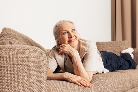 Dreaming senior woman on a sofa  Aged female looking away and smiling in the living room