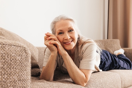 Portrait of a senior woman with grey hair lying on a sofa and looking at a camera