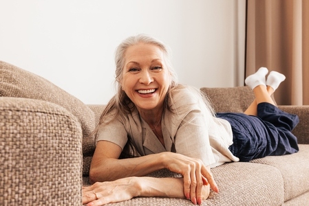 Close up of a happy senior woman lying on a sofa and looking at camera