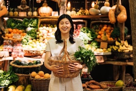 Asian woman with closed eyes holding a basket while standing at outdoor market