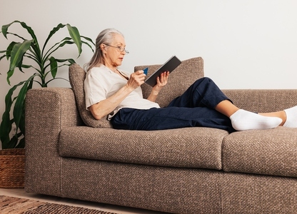 Side view of a senior female holding a credit card and digital tablet  Aged woman renew subscription
