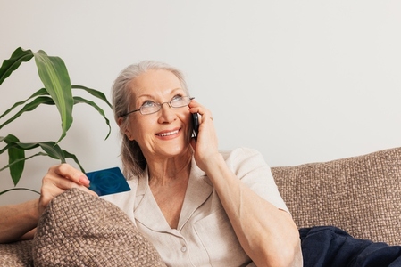 Smiling senior woman ordering through a cell phone  Aged female in eyeglasses holding a credit card while lying on a sofa