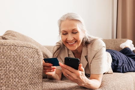Close up of a senior female holding a credit card and smartphone  Adult smiling woman making a purchase with smartphone at home