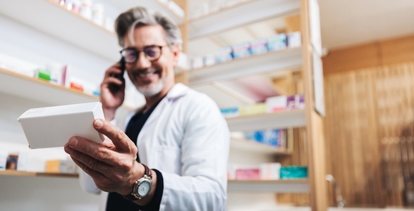 Drug store pharmacist holding a medication box and talking to a patient on the phone