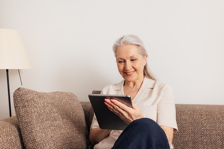 Aged woman with grey hair using a digital tablet at home