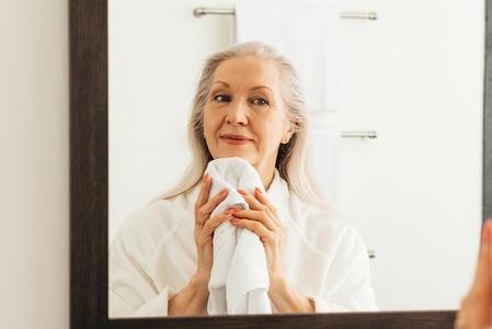 Senior woman with grey hair wiping her chin in front of a mirror