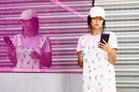 Young Asian female using smartphone near reflective wall