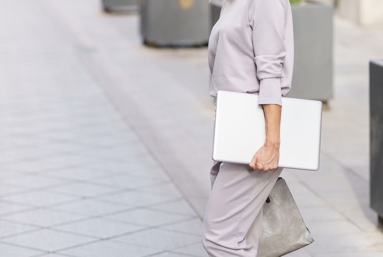 Confident well dressed businesswoman with netbook strolling in city