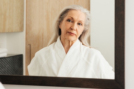 Aged woman with grey hair looking at her reflection in mirror