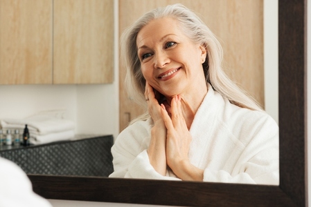 Cheerful woman with grey hair admires her reflection in a mirror