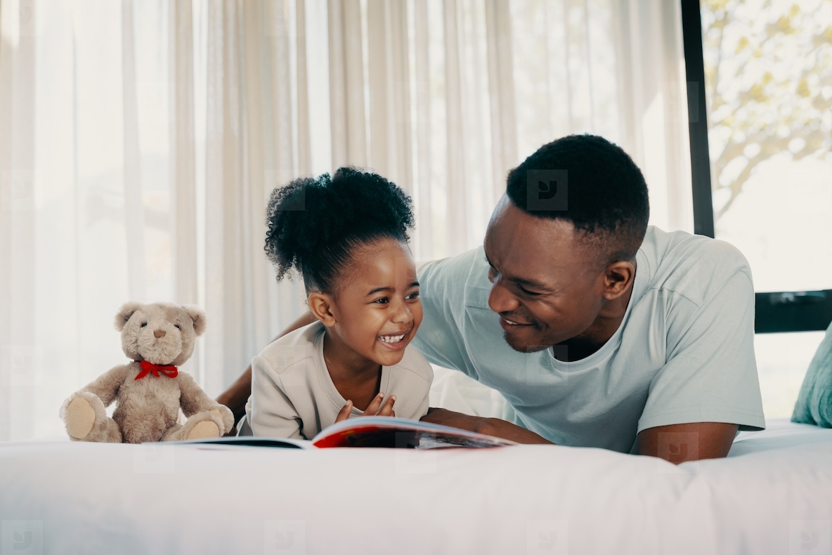 Happy child enjoying a story book with her dad